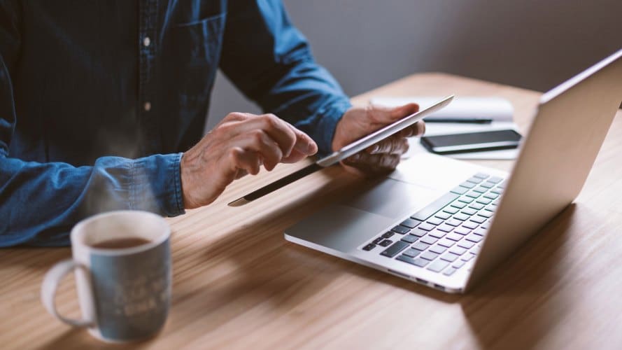 persona incorpórea sosteniendo una tableta mientras también usa su computadora portátil