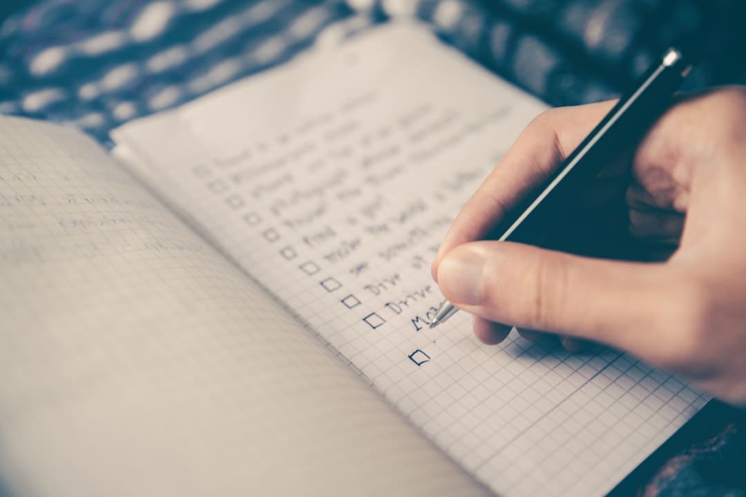 Mano escribiendo lista en cuaderno cuadriculado.