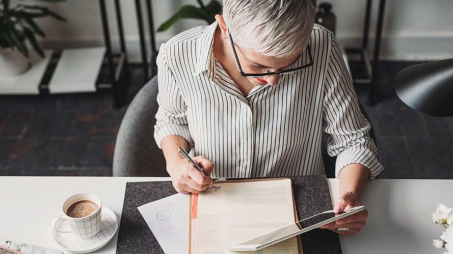 Mujer mayor sentada en el escritorio mirando la tableta mientras toma notas sobre el futuro de la experiencia del empleado