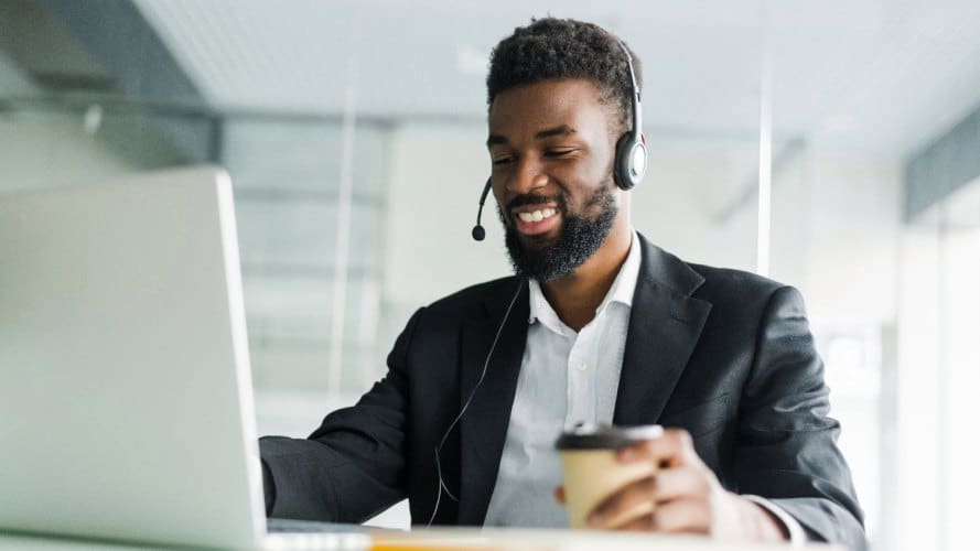 Agente de servicio al cliente con auriculares y café en una mano mirando la pantalla de su computadora portátil: automatice los procesos comerciales: TI, CIO